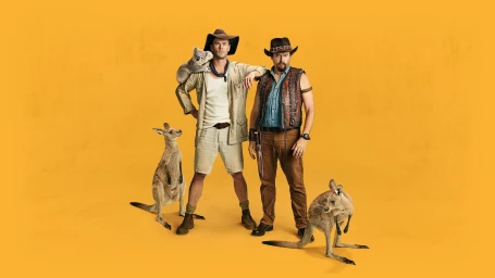 Chris Hemsworth and Danny McBride in outback attire posing with kangaroos and a koala against a solid yellow backdrop