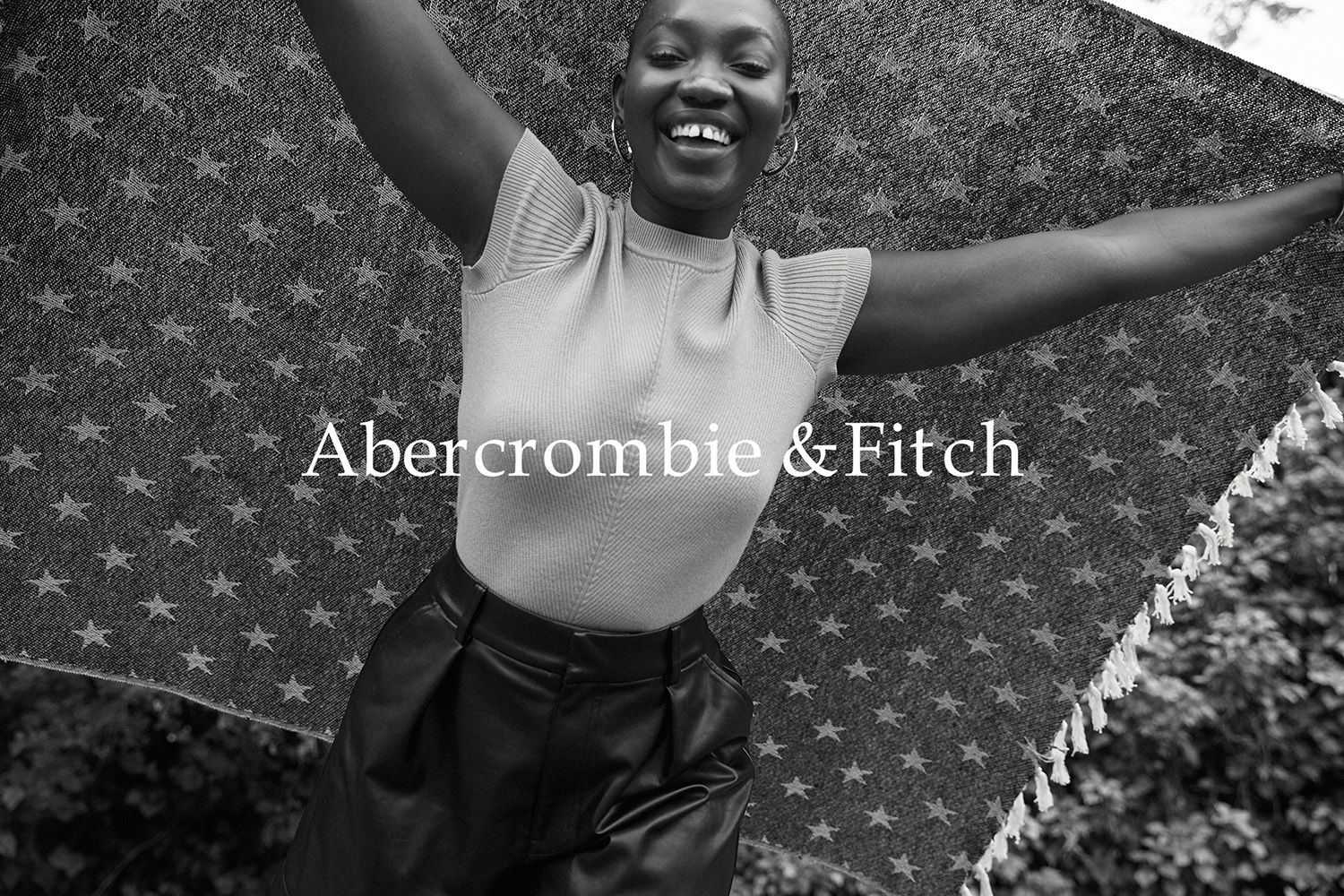 Smiling Black woman holding a star patterned blanket overhead with both arms raised outdoors