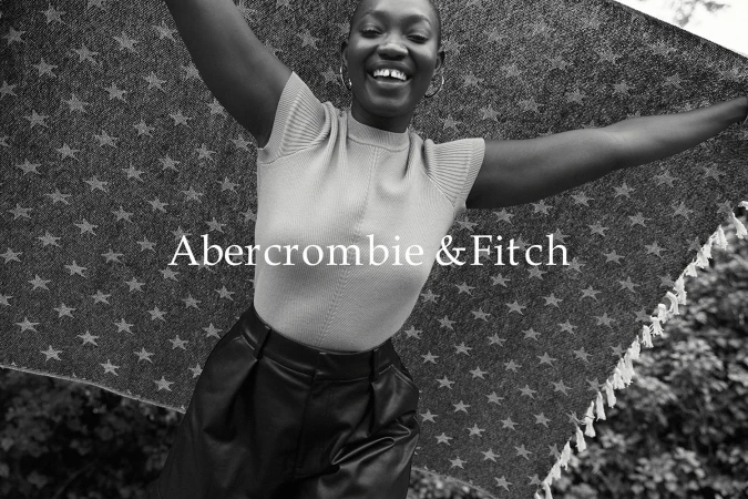 Smiling Black woman holding a star patterned blanket overhead with both arms raised outdoors