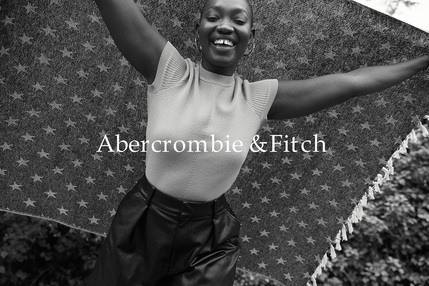 Smiling Black woman holding a star patterned blanket overhead with both arms raised outdoors