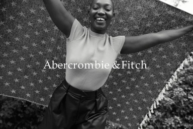 Smiling Black woman holding a star patterned blanket overhead with both arms raised outdoors