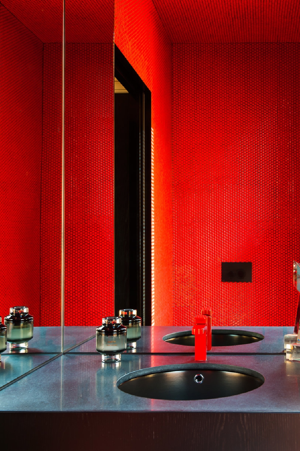 Red bathroom interior featuring a dark countertop with black sink, grey bottles, red soap dispenser and mirror reflecting the scene.
