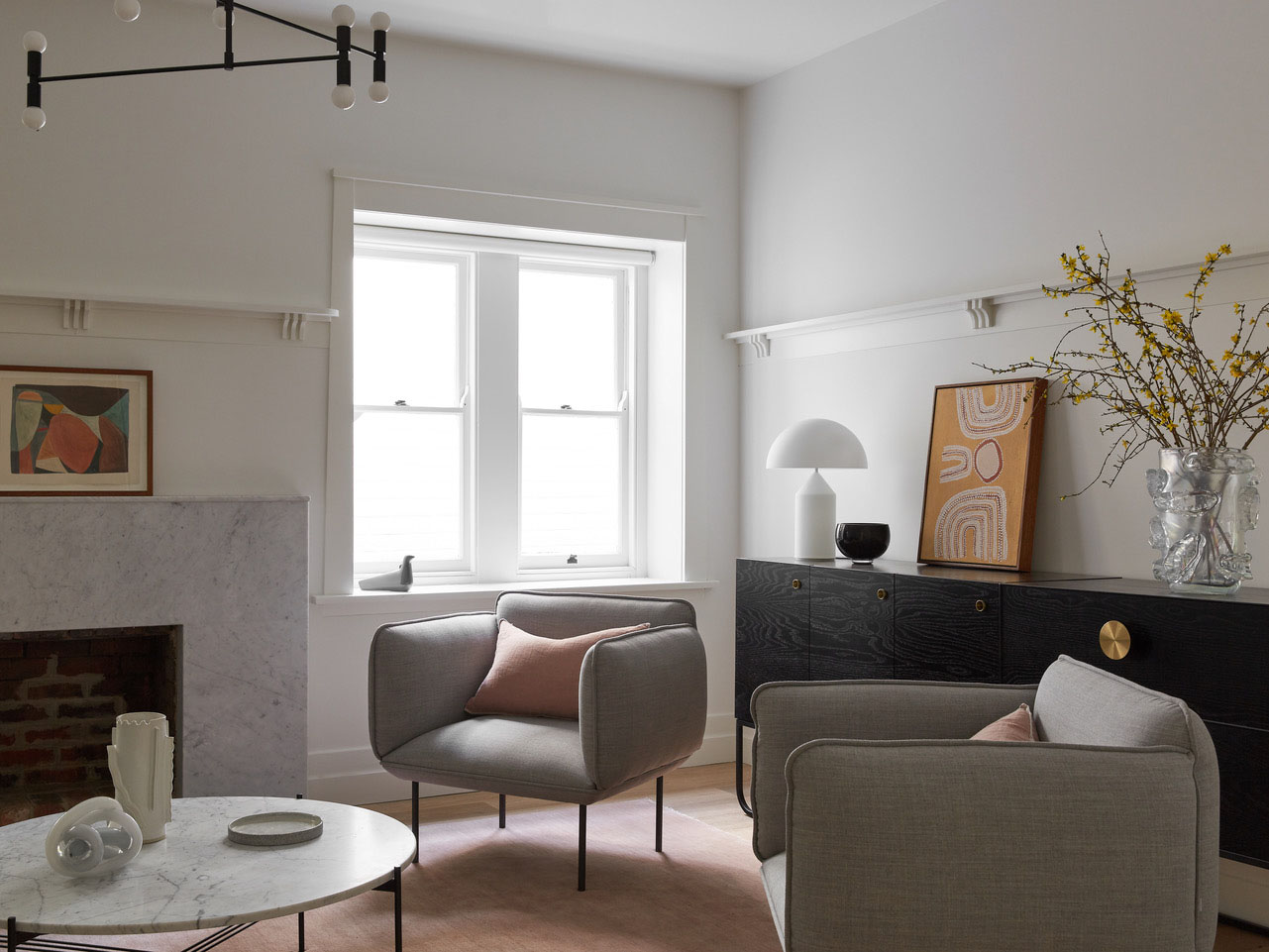 Living room interior featuring two gray armchairs, marble coffee table, black sideboard, neutral walls, and natural light from a window.