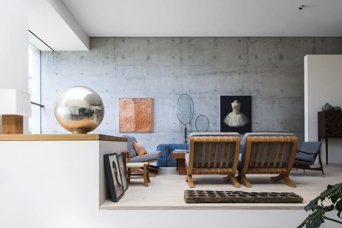 Living room interior featuring concrete walls, modern furniture, and artwork, creating a minimalist and artistic ambiance with natural light.
