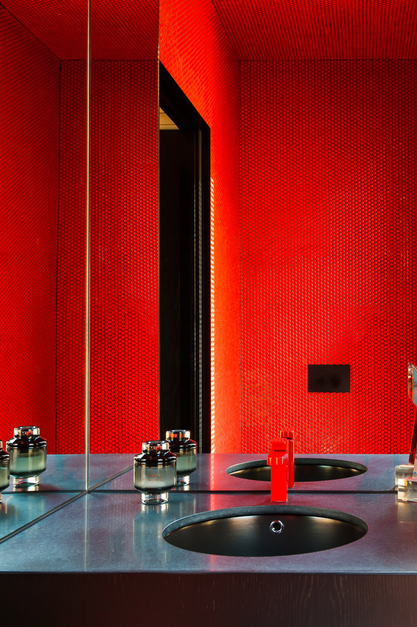 Sleek bathroom interior featuring red honeycomb tile walls, a dark countertop with an oval sink, a bright red faucet, and glass decor.