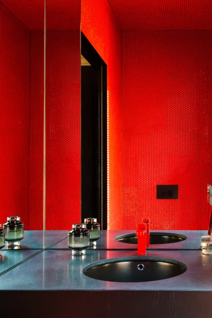 Sleek bathroom interior featuring red honeycomb tile walls, a dark countertop with an oval sink, a bright red faucet, and glass decor.