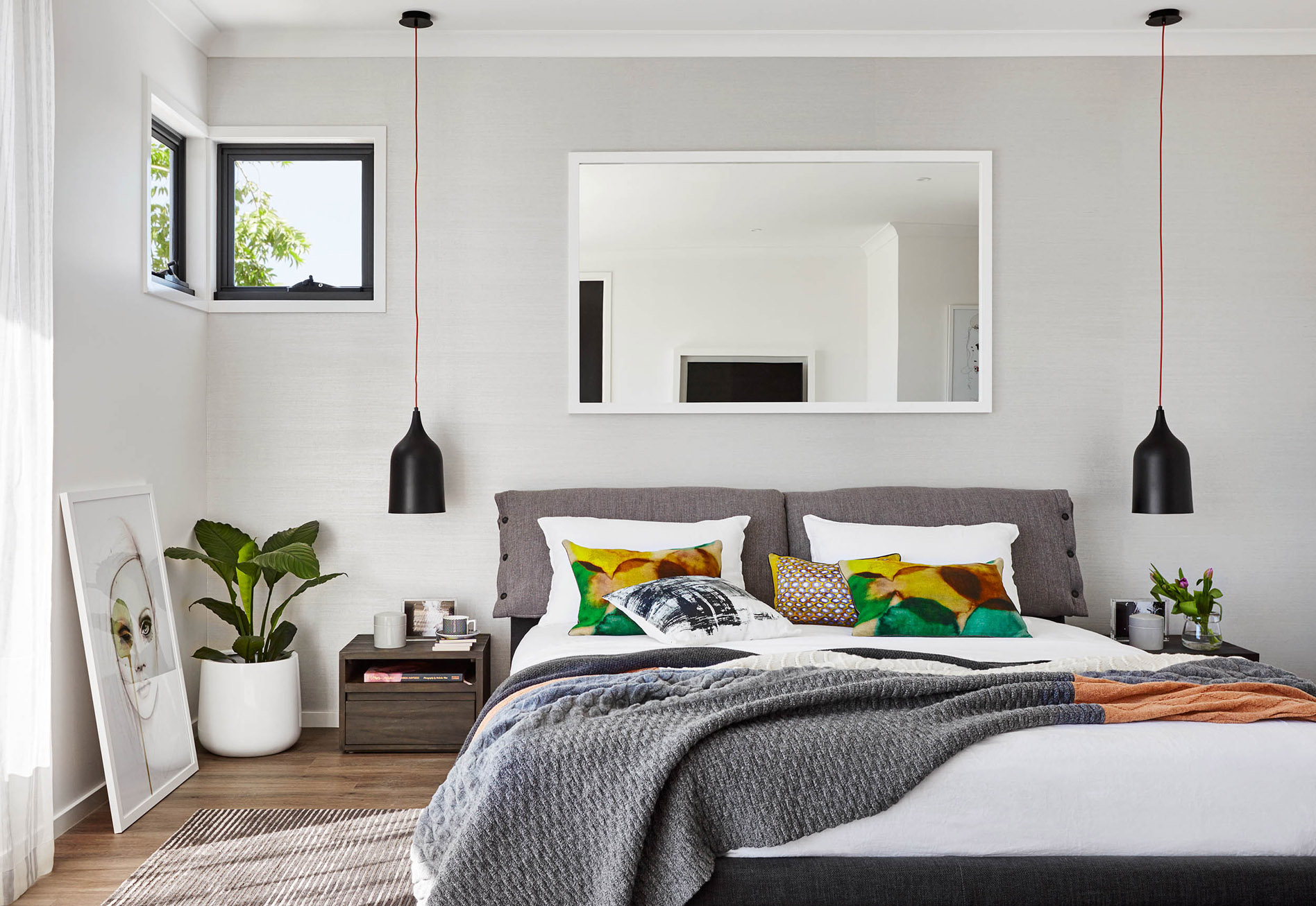 Bedroom interior featuring a bed with a grey headboard, colorful pillows, a grey throw, and pendant lighting in a modern design.