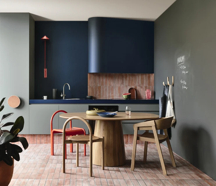 Stylish kitchen interior featuring a round wooden table, colorful chairs, modern cabinetry, and muted wall colors in a residential setting.