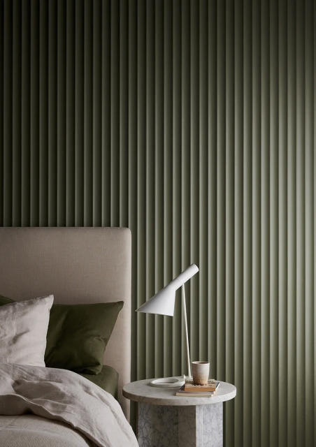 Interior shot of a bedroom with a bed featuring neutral-colored bedding and pillows, set against a vertically ridged green wall.