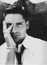 Monochrome portrait of a man in a white shirt and tie posing with his hand on his face.
