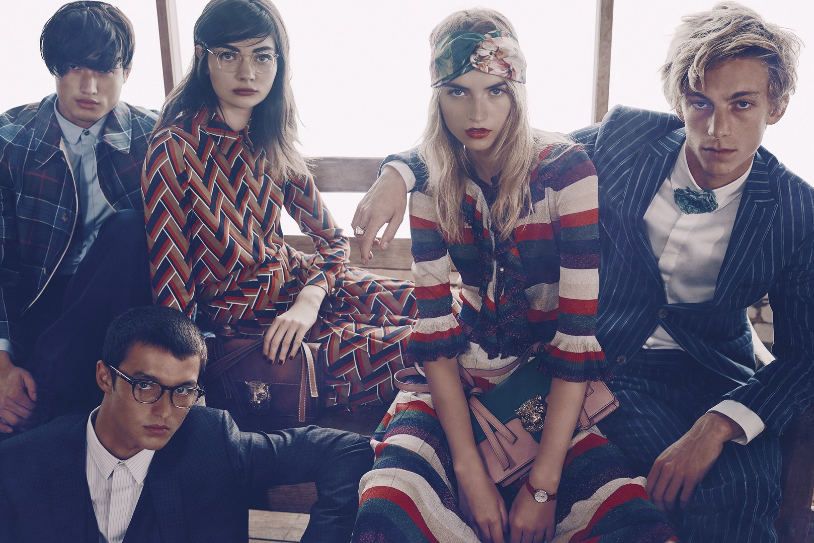Group of five young adult fashion models posing indoors, wearing stylish suits and dresses in a fashion editorial-style photo.