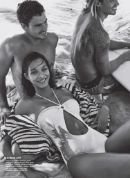 Monochrome beach editorial featuring a smiling woman in a halter swimsuit with two men nearby on sandy terrain.