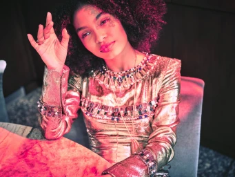 Close-up portrait of a woman wearing an ornate metallic gold dress and jewelled collar under vibrant pink lighting by photographer Beau Grealy.