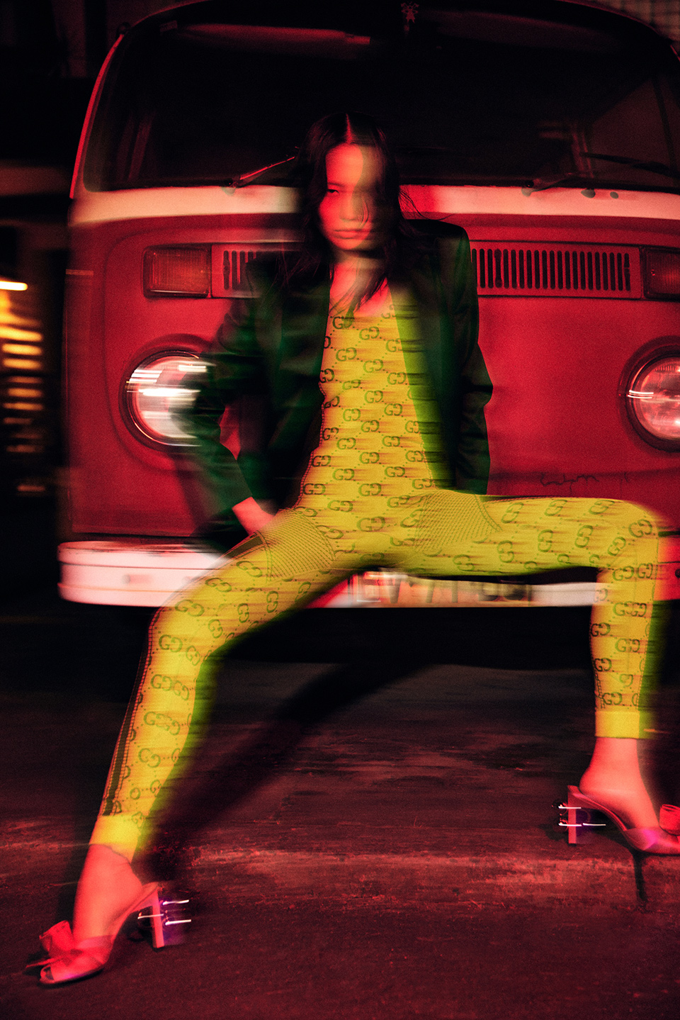 A woman in a patterned outfit poses in front of a red VW bus, shot with motion blur and low lighting for a dynamic fashion image.