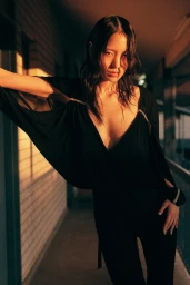 Asian woman in black dress leaning against railing in warm sunset light styled by Jana Bartolo in Sydney