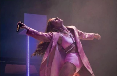 Performer in a pink outfit with a pearl body chain holding a microphone under dramatic stage lighting styled by Jana Bartolo