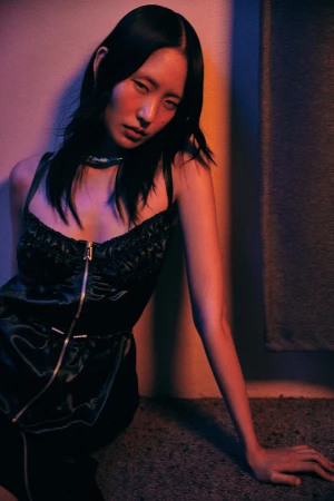 East Asian woman in black zip-front dress under dramatic orange and blue lighting