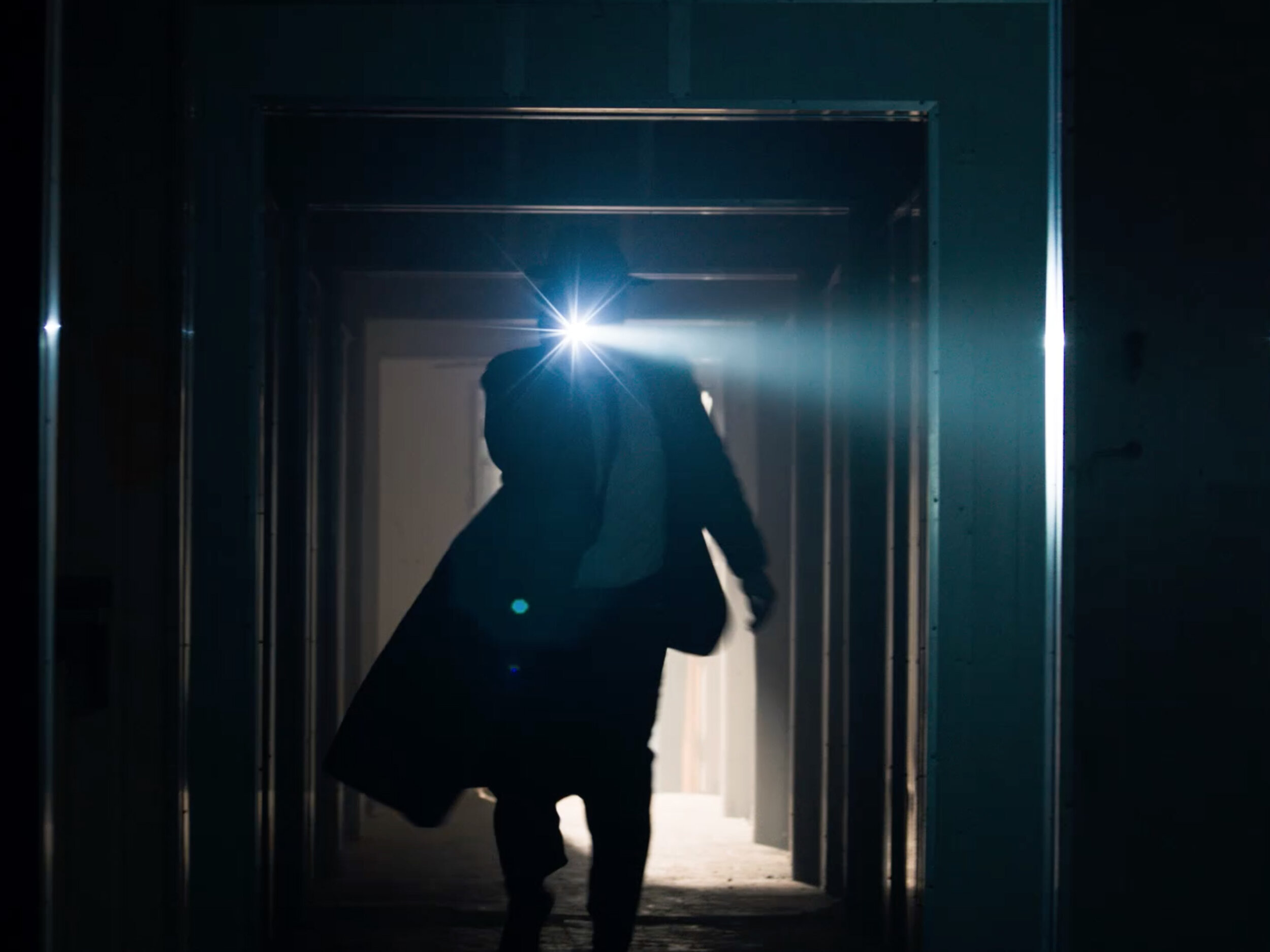 Silhouette of person walking through a hallway with a bright light in dark lighting. Interior architecture with corridor design.