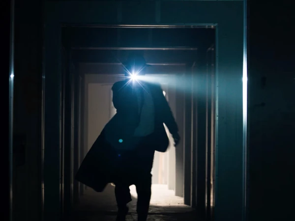 Silhouette of person walking through a hallway with a bright light in dark lighting. Interior architecture with corridor design.