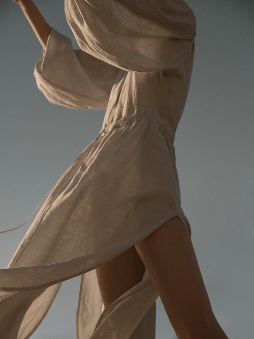 Woman in flowing linen dress against blue sky. Fashion, style, summer vibes, elegance, and simplicity captured in an outdoor setting.