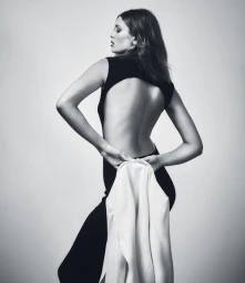 Model in a black backless jumpsuit holding a light jacket in a studio by photographer Anne Peeters