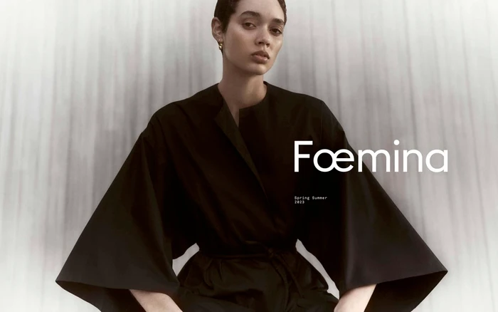 Model in black kimono-style dress with wide flared sleeves posing against a textured grey background