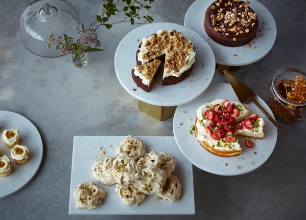 Overhead shot of an assortment of desserts, including cakes, meringues, and cupcakes, displayed on marble serving plates and cake stands.