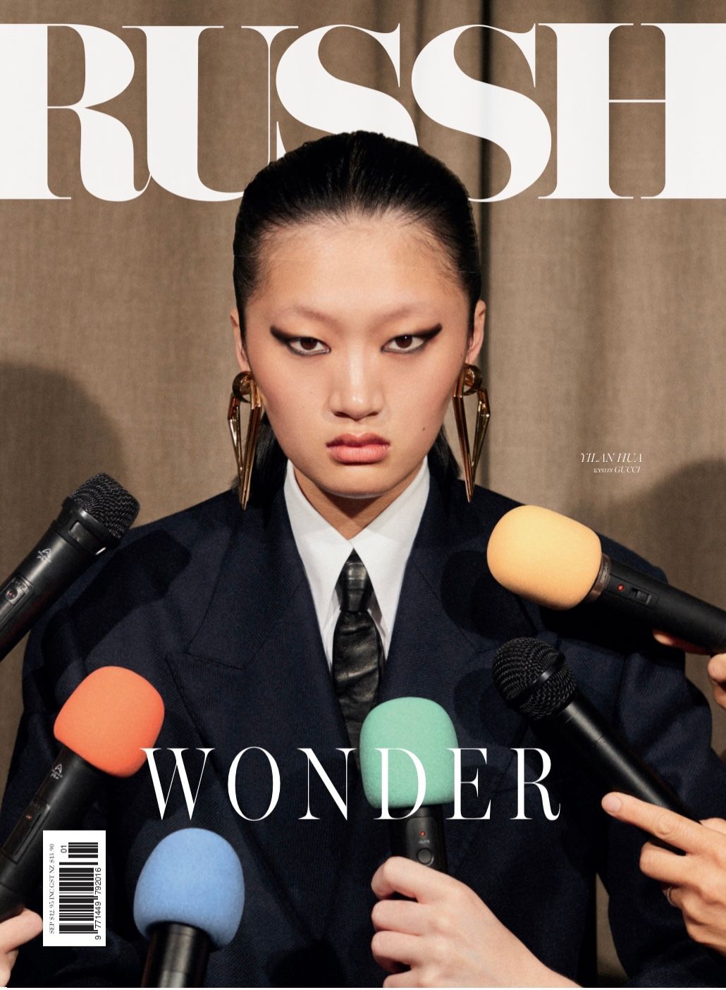 Magazine cover featuring a young Asian woman wearing a suit and statement earrings, surrounded by microphones. The background is tan.