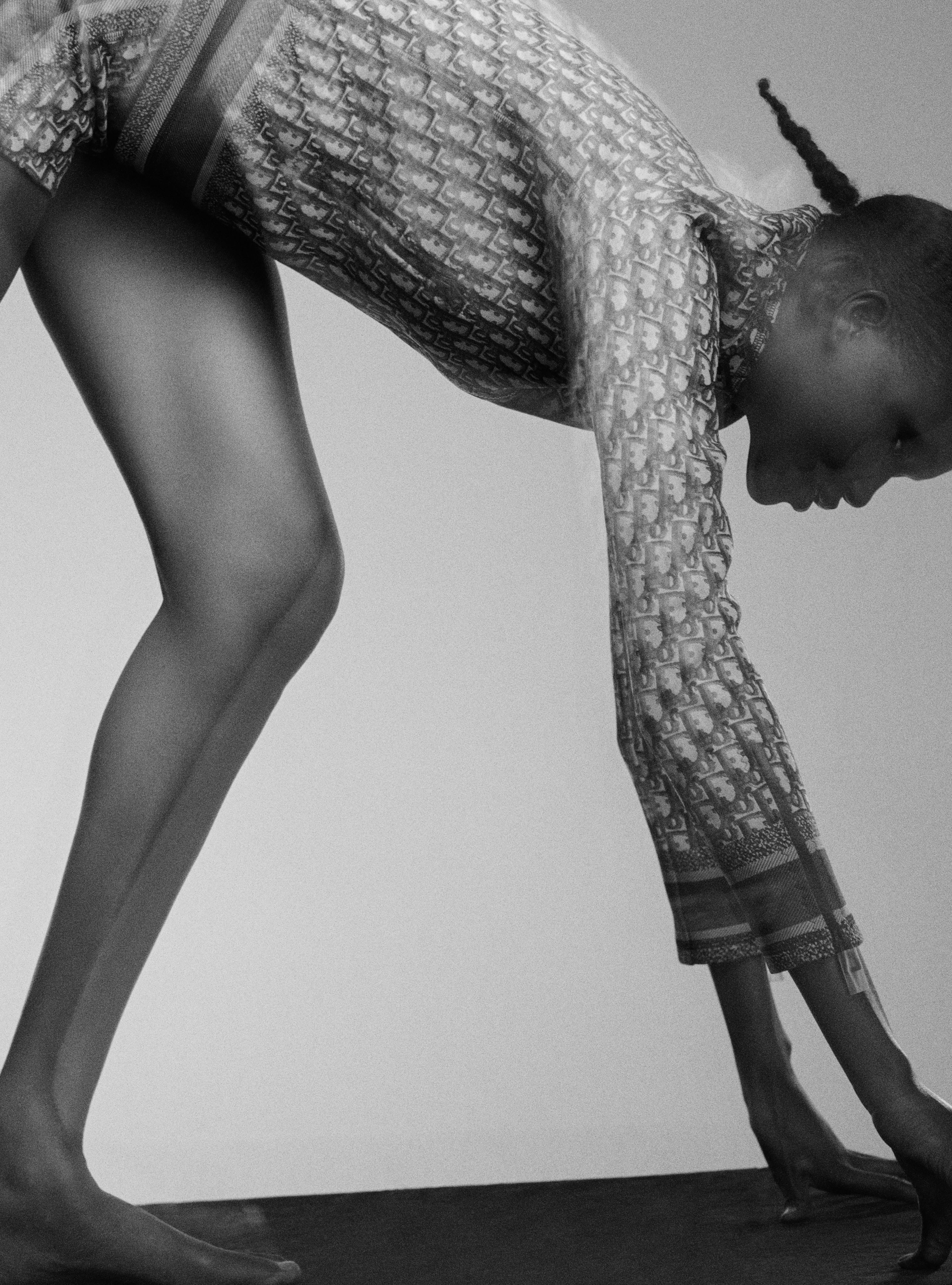 Monochrome shot of a woman bending forward, clad in patterned top and tights, showcasing a sleek and artistic studio portrait.