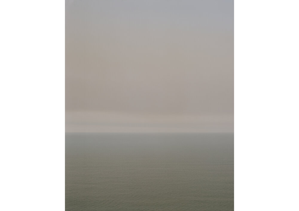 Atmospheric seascape featuring a hazy sky over the ocean, with muted colors and a sense of tranquility and natural beauty.