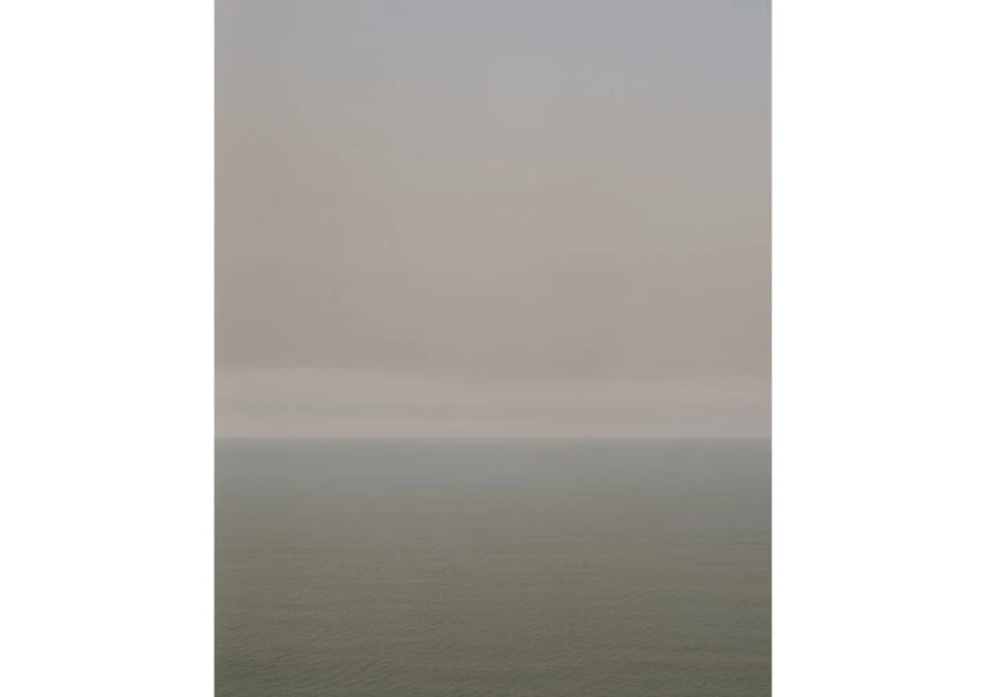 Atmospheric seascape featuring a hazy sky over the ocean, with muted colors and a sense of tranquility and natural beauty.