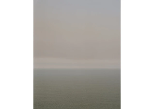 Atmospheric seascape featuring a hazy sky over the ocean, with muted colors and a sense of tranquility and natural beauty.