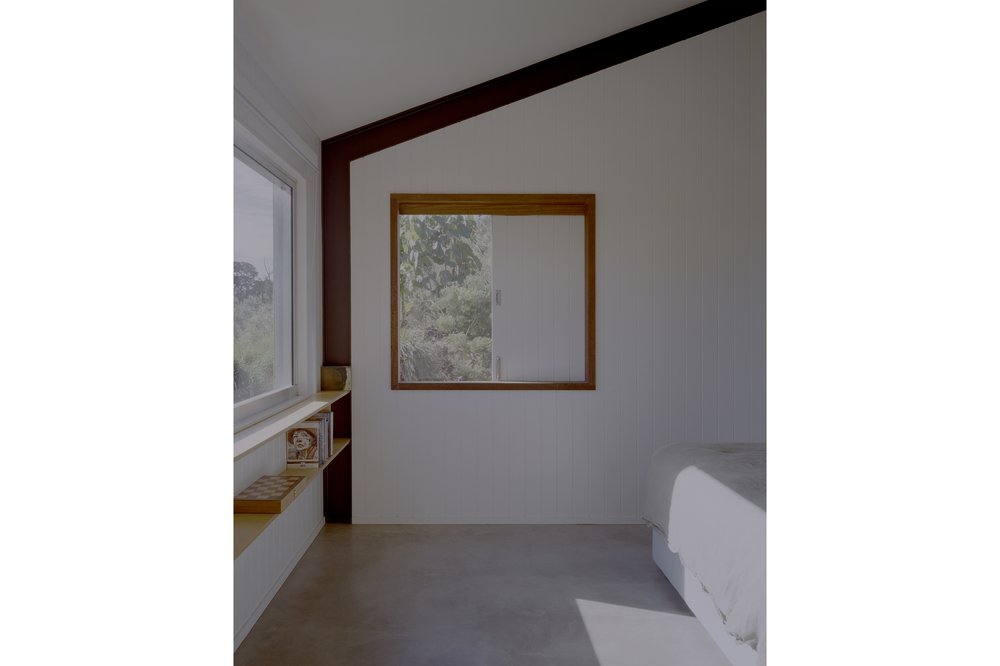 Minimalist bedroom interior featuring natural light from two windows, concrete floors, white walls, and light-colored bed, creating a serene space.