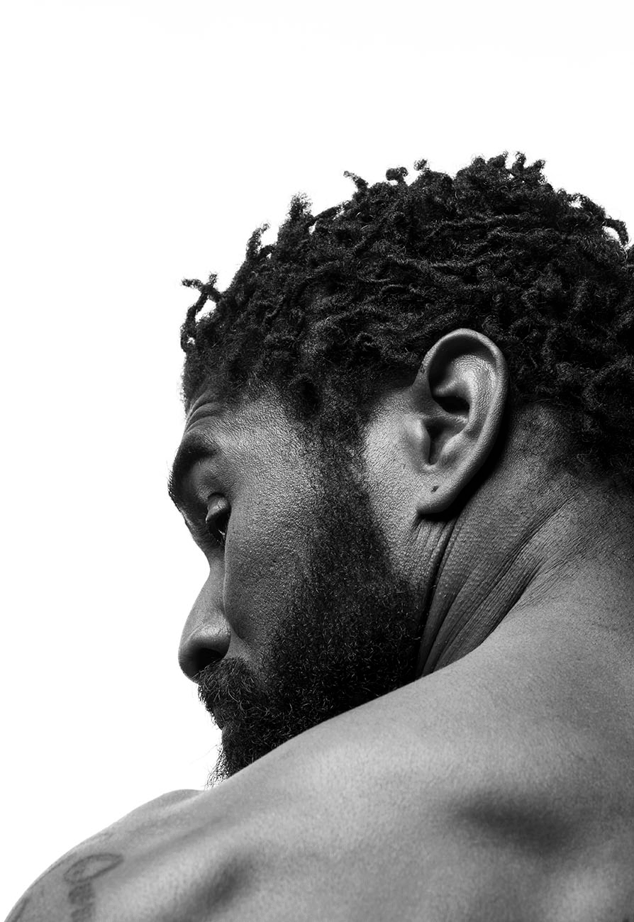 Striking black and white portrait of muscular African American male screaming with torso tattoos set against a bright white background.