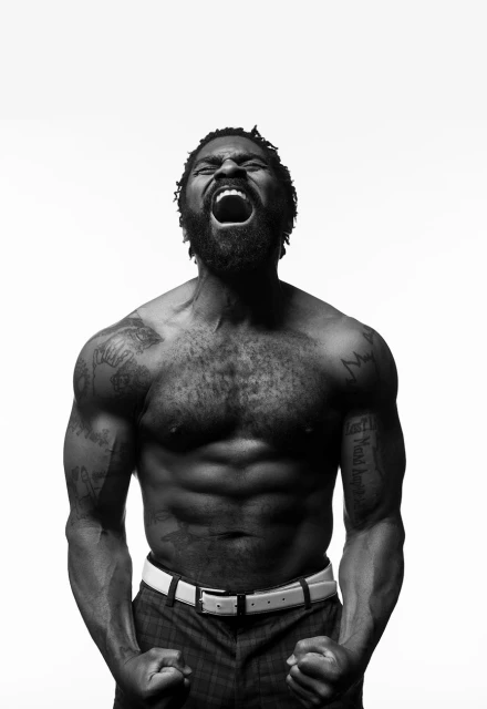 Striking black and white portrait of muscular African American male screaming with torso tattoos set against a bright white background.