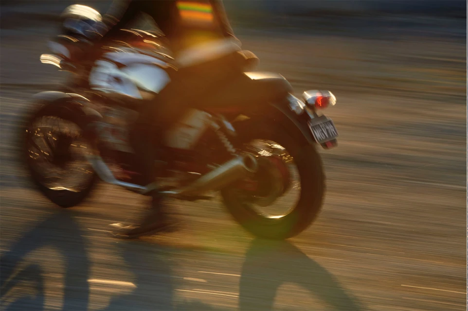 Motion blur of a motorcycle with a rider on a paved road with golden sunlight creating shadows, capturing speed and movement.