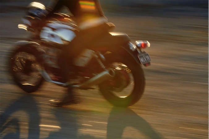 Motion blur of a motorcycle with a rider on a paved road with golden sunlight creating shadows, capturing speed and movement.