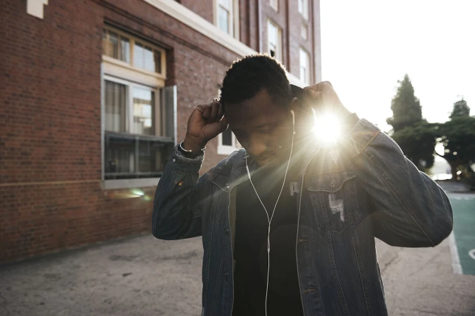 Black man wearing a denim jacket adjusting his hood against a brick building exterior in Sydney