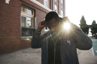 Black man wearing a denim jacket adjusting his hood against a brick building exterior in Sydney