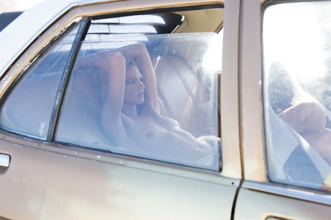 Woman lying inside the back seat of a vintage car with her arms raised behind her head, photographed by Ian & Erick.