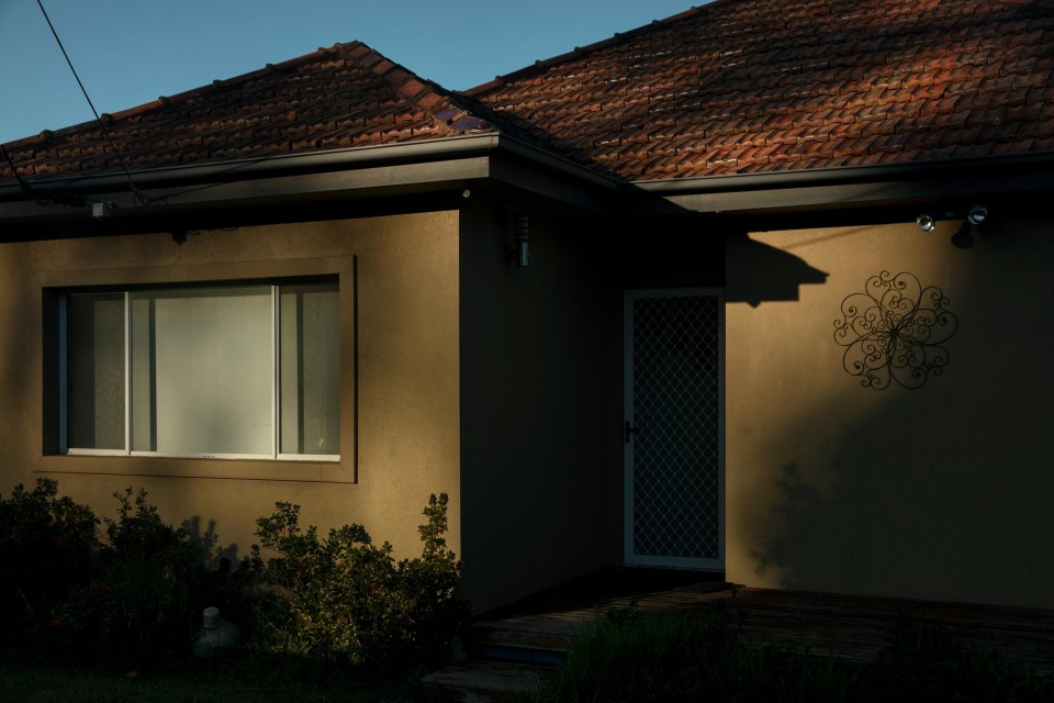 Exterior of a single-story home with a dark brown tiled roof, neutral siding, and a security door, under a clear, bright sky.