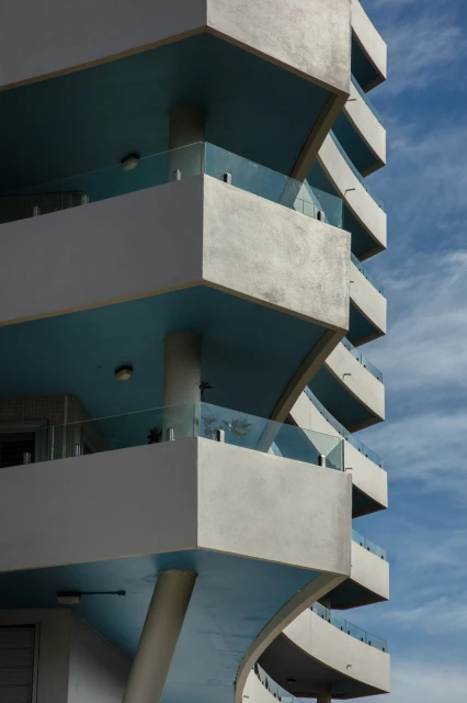 Exterior of modern high-rise building with geometric balcony design and white and blue color scheme against a partly cloudy sky.