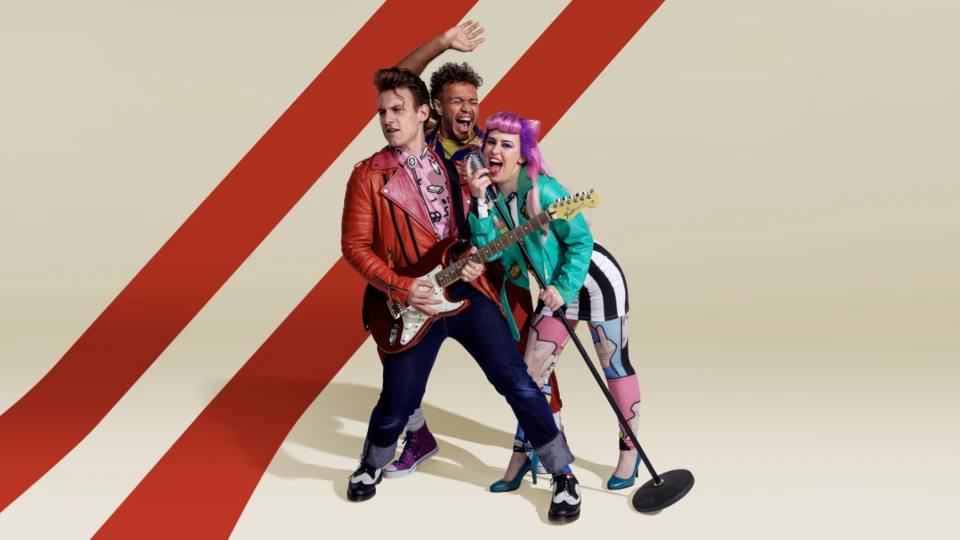 Music band performs with a guitarist in a red jacket, a vocalist in a turquoise jacket, and a background vocalist with hand raised.