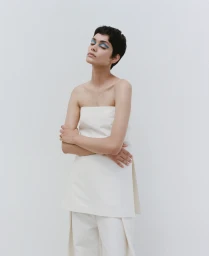 Model with short dark hair and blue eyeshadow wearing a strapless white top against a neutral background
