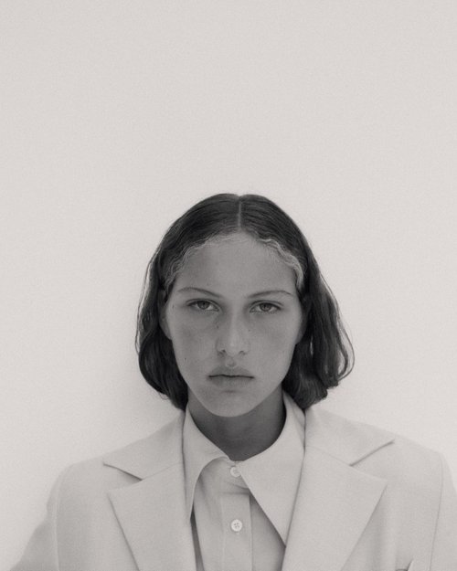 Monochrome portrait of a young adult woman with dark hair, wearing a light-colored blazer and button-down shirt against a white background.