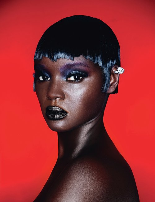 Close-up portrait of a Black female fashion model with short black hair, dramatic eyeshadow, and dark lipstick against a red backdrop.