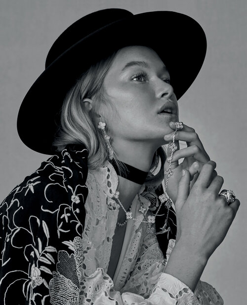A woman with blonde hair wears a black hat and elegant jewelry, posing in a black and white fashion portrait.