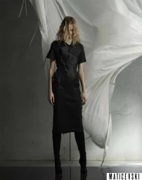 Model standing in a black dress and high boots against a concrete wall with billowing white fabric.