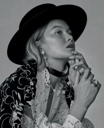 Monochrome portrait of a woman in a wide-brimmed black hat, lace blouse, choker necklace, and floral patterned jacket.