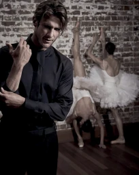 Man in black shirt with two ballet dancers in white tutus against brick wall